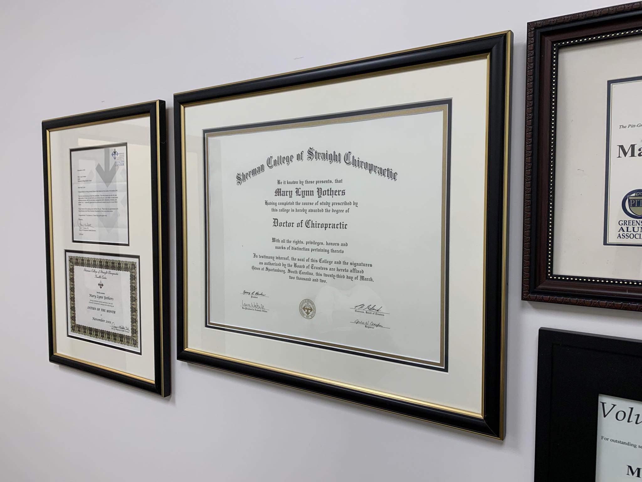 Framed diplomas and certifications on the office wall, including Dr. Yothers' Doctor of Chiropractic degree from Sherman College