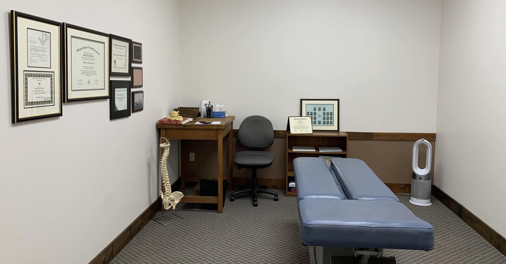 Chiropractic treatment room with adjusting table and framed credentials on the wall